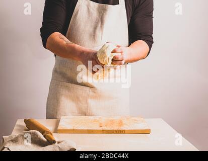 A man in an apron kneads the dough makes bread. The concept of home-made baking. Selective focus. Stock Photo