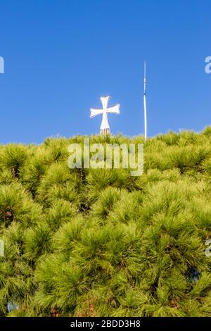 Beautiful white cross of the Orthodox church of the Monastery of St. Nicholas, lake Vistonida, Porto Lagos, Xanthi region, Northern Greece, bell tower partial view against clear blue sky, green trees Stock Photo