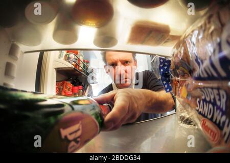 17.03.2020, Berlin, Berlin, Germany - A man puts a bottle of beer in his well-stocked fridge. 00S200317D604CAROEX.JPG [MODEL RELEASE: NO, PROPERTY REL Stock Photo