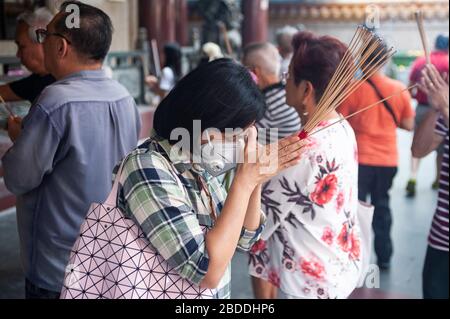 06.03.2020, Singapore, , Singapore - A woman holds smoking sticks in her hands and prays at the Kwan Im Thong Hood Cho Temple. She is wearing a respir Stock Photo