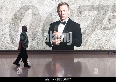 12.03.2020, Singapore, , Singapore - One man is walking past an advertising space for the new James Bond movie and is wearing a respirator to protect Stock Photo