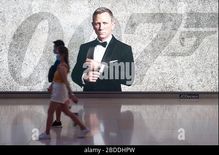 12.03.2020, Singapore, , Singapore - Two people are walking past an advertising space for the new James Bond movie, wearing a respirator to protect th Stock Photo