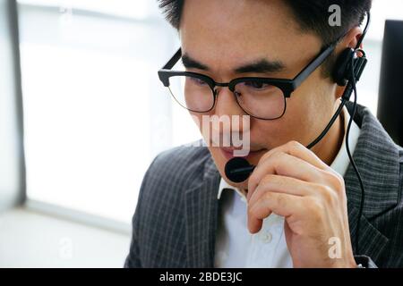 Portrait of Confident Asian customer support, operator, call center or sales agent man is holding his headset while talking with customer Stock Photo