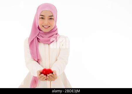 Portrait of Muslim woman in hijab holding red heart with a beautiful smile, isolated white background with copy space Stock Photo