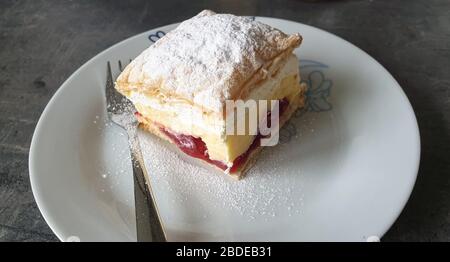 Sweet cream cake on a plate with a layer of strawberry jam and sprinkled with powdered sugar Stock Photo