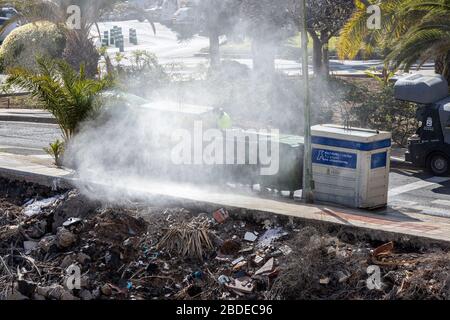 Council worker with jet washer cleaning and disinfecting the rubbish bins,  Playa San Juan, Tenerife, Canary Islands, Spain Stock Photo