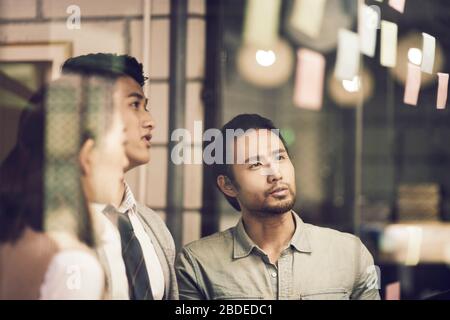 three asian small company businesspeople young entrepreneurs meeing discussing in office using sticky notes Stock Photo