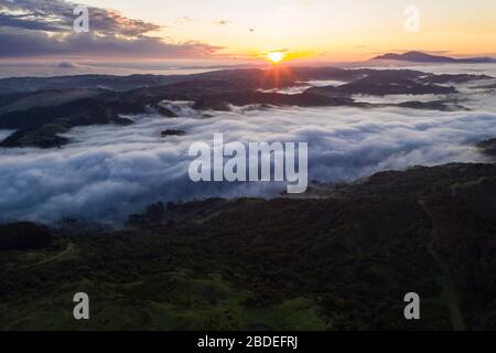 A beautiful sunrise illuminates fog as it rolls through valleys in Northern California. Just west of these hills and valleys is San Francisco Bay. Stock Photo