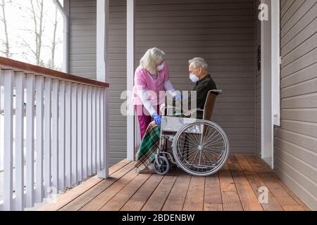 Woman and man in wheelchair wearing protective mask to prevent coronavirus transmission on porch Stock Photo