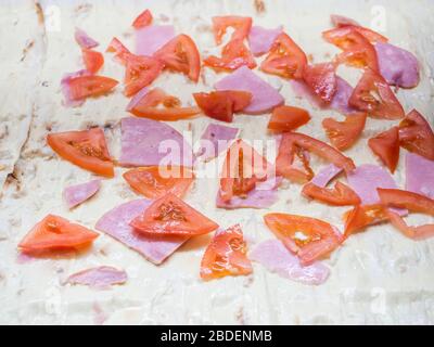Slices of ripe red tomatoes and slices of ham laid out on a light baking dough Stock Photo