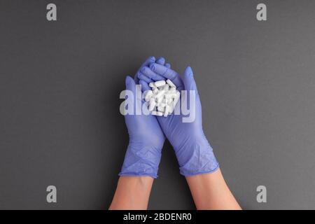 Female hands in purple color latex rubber glove holds in palms of handful of medicines, tablets, pills on gray background, copy space, flat lay Stock Photo