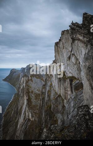 Norway, Senja, Man sitting on the edge of steep cliff on top ofÂ SeglaÂ mountain Stock Photo