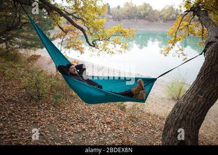 Italy, Smiling man lying in hammock near lake Stock Photo