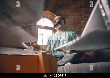 Paperwork. Young man doing yoga at home while being quarantine and freelance online working. Remote office, isolated. Concept of healthy lifestyle, wellness, being safe while coronavirus pandemic. Stock Photo