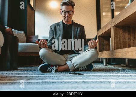 Businessman sitting on floor and meditating in yoga pose. Mature businessman doing relaxation yoga in office lounge. Stock Photo