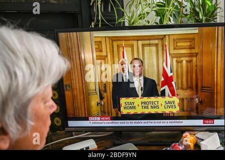 Dominic Raab giving a televised press conference on Covid-19, with Chris Whitty (Chief Medical Officer), watched by an older woman. Stock Photo