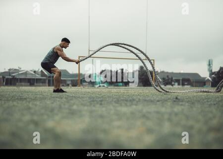 Fitness man using training ropes for exercise outdoors at a ground. Athlete working out with battle ropes outdoors. Stock Photo