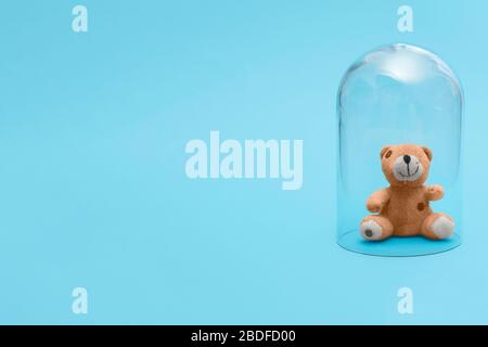 Children kid stuffed cuddly toy bear in quarantine under a glass cloche dome on a blue background with copy space and room for text Stock Photo