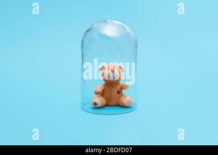 Children kid stuffed cuddly toy bear in quarantine under a glass cloche dome on a blue background with copy space and room for text Stock Photo