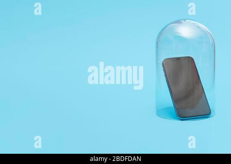 Mobile smartphone in quarantine under a glass cloche dome on a blue background with copy space and room for text Stock Photo