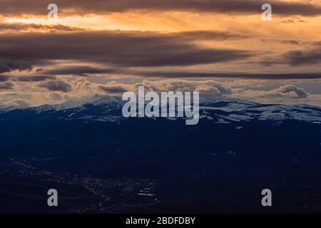 Beautiful landscape of mountains in a orange sky with lots of clouds over a small city Stock Photo