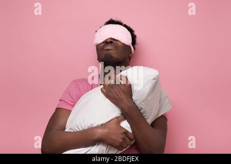 Sleepy dark haired man in mask holding white pillow Stock Photo