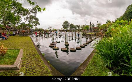 Horizontal view of tourists walking over the stepping stones at the Tirta Gangga water palace in Bali, Indonesia. Stock Photo