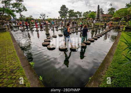 Horizontal view of tourists walking over the stepping stones at the Tirta Gangga water palace in Bali, Indonesia. Stock Photo