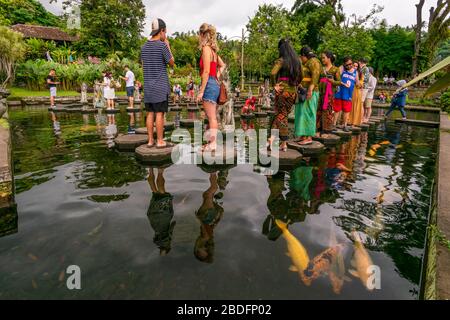 Horizontal view of tourists walking over the stepping stones at the Tirta Gangga water palace in Bali, Indonesia. Stock Photo