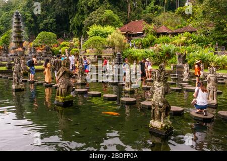 Horizontal view of tourists walking over the stepping stones at the Tirta Gangga water palace in Bali, Indonesia. Stock Photo