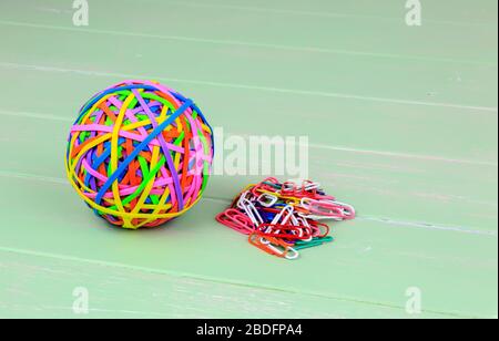 Coloured ball of rubber bands and paper clips on a green shabby board back ground Stock Photo