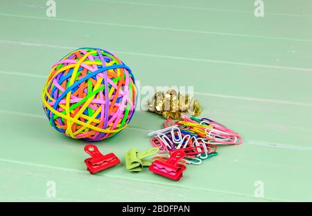 Coloured ball of rubber bands paper clips and drawing pins on a green shabby board back ground Stock Photo