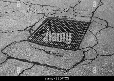 Drainage sewer grate on worn and cracked asphalt street Stock Photo