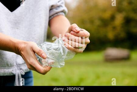 Woman stuffing soft waste plastics into large plastic bottle to make an ecobrick which can then be used as a buiding block Stock Photo