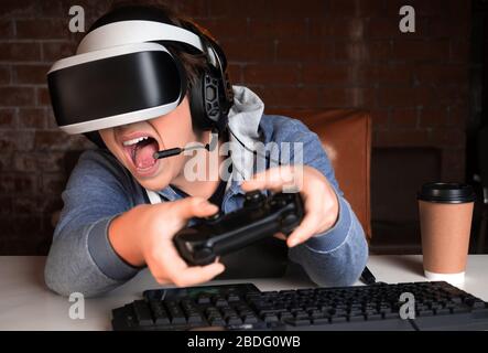 Teenager in VR and headphones with microphone playing a game at home and streaming. The madman shouted during his last and hardest battle. Stock Photo