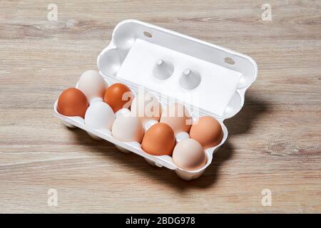 eggs of different shades from white to brown are packed together in one egg crate on a wooden table surface Stock Photo