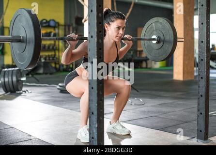 Photo of a woman is lifting weight while working out with barbell in gym. Healthy lifestyle concept. Stock Photo