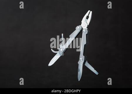 Multi-functional tool on a black textural background. Stock Photo