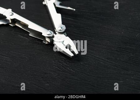 Multi-functional tool on a black textural background. Stock Photo