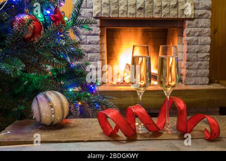 Christmas eve. Two empty glasses of champagne wine before Christmas tree decorated toys and christmas lights near cozy fireplace, in country cottage. Stock Photo