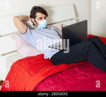 Sick man with medical mask using tablet pc in bed. Home quarantine concept. Stock Photo
