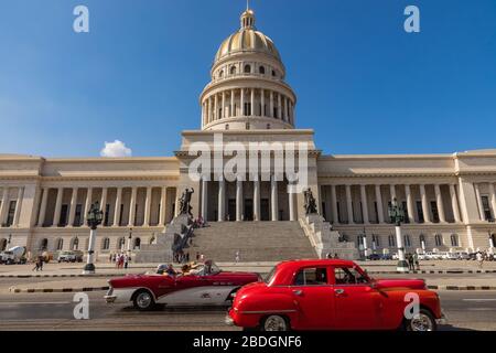 HAVANA, CUBA - DECEMBER 10, 2019: Brightly colored classic American cars serving as taxis pass on the main street in front of the Capitolio building i Stock Photo