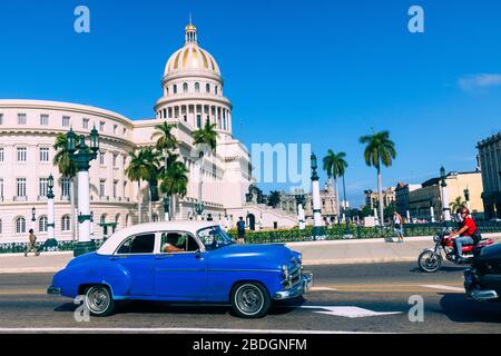 HAVANA, CUBA - DECEMBER 10, 2019: Brightly colored classic American cars serving as taxis pass on the main street in front of the Capitolio building i Stock Photo