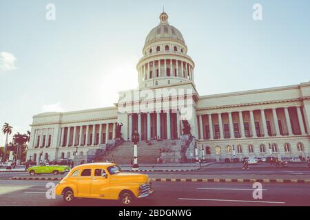 HAVANA, CUBA - DECEMBER 10, 2019: Brightly colored classic American cars serving as taxis pass on the main street in front of the Capitolio building i Stock Photo