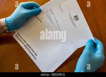 Man wearing surgical gloves holding HM Government letter from Boris Johnson about Covid-19 Coronavirus, United Kingdom