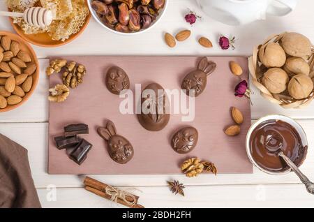 Home made chocolate easter eggs in the shape of a rabbit and chicken on a wooden white background with melted chocolate and nuts. Preparing for Easter Stock Photo