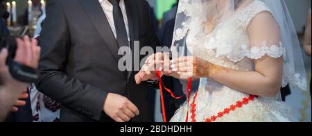 Left hand. Bride is wearing a ring on the hands of a man . Close up shoot of groom's hand putting a wedding ring on the bride's finger. Stock Photo