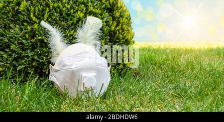 Easter Egg as Rabbit Head with feather ears and corona protection mask in the lawn. Stock Photo
