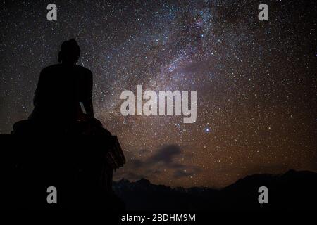 Buddhist temple beneath night sky stars in Himalayas. Statue of Buddha in meditation beneath Milky Way galaxy in mountains of Nepal Stock Photo