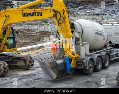 PORTHCAWL, WALES - JUNE 2018: Concrete mixer unloading ready mixed concrete into the bucket of a heavy duty excavator for sea defences Stock Photo